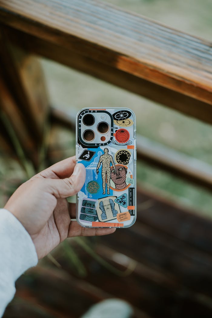 A close-up of a hand holding a creatively designed smartphone case outdoors, featuring various colorful elements.