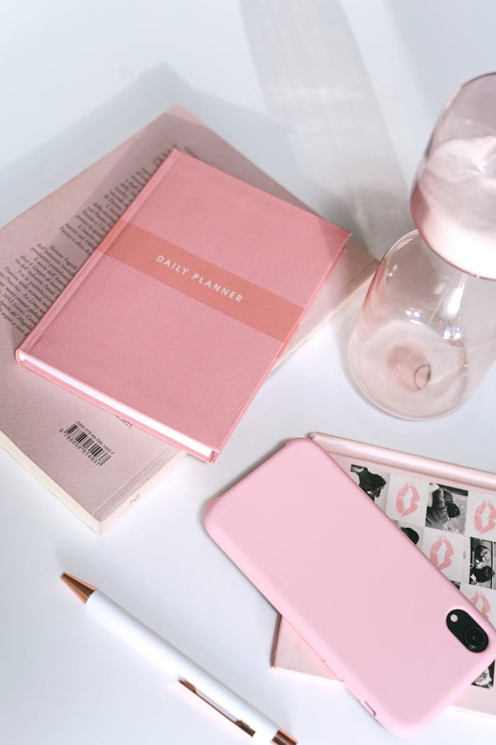Modern pink-themed desk layout featuring a planner, phone, pen, and accessories.